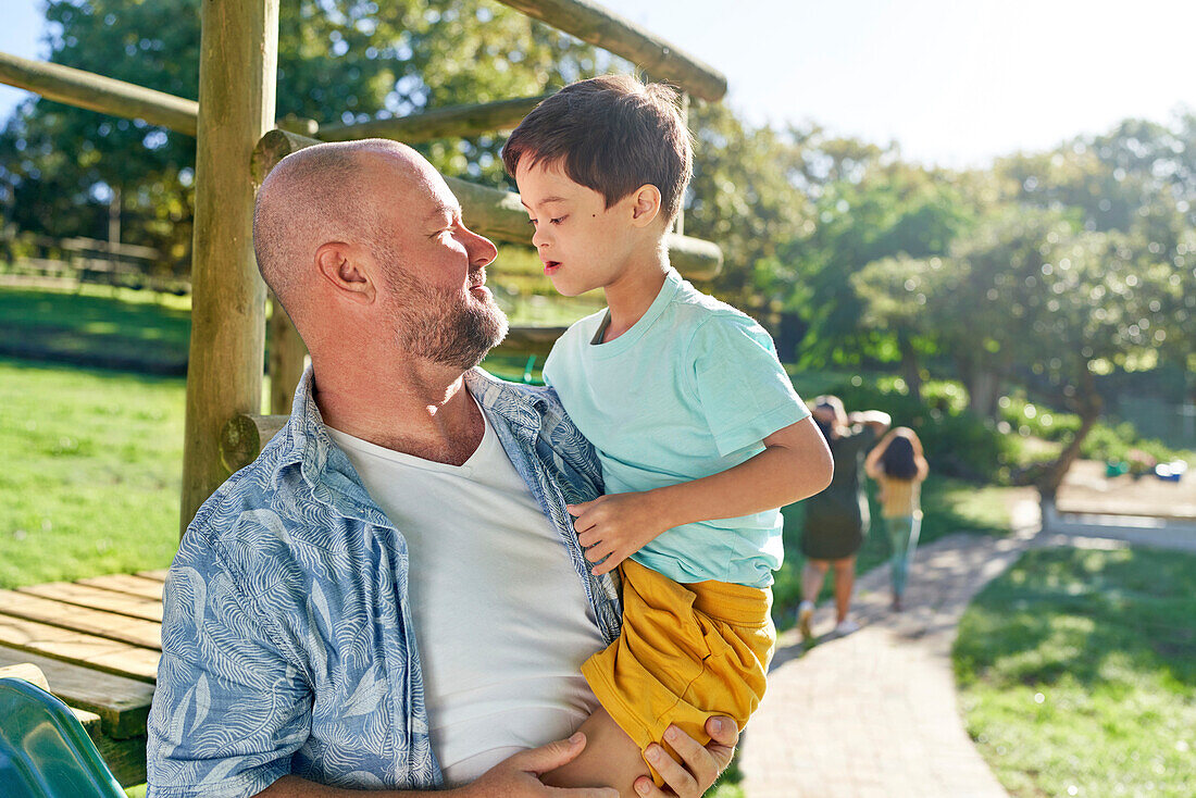 Father holding son with Down syndrome in sunny park