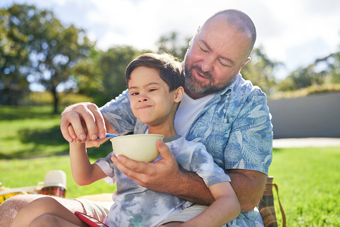 Father feeding son with Down syndrome in summer park