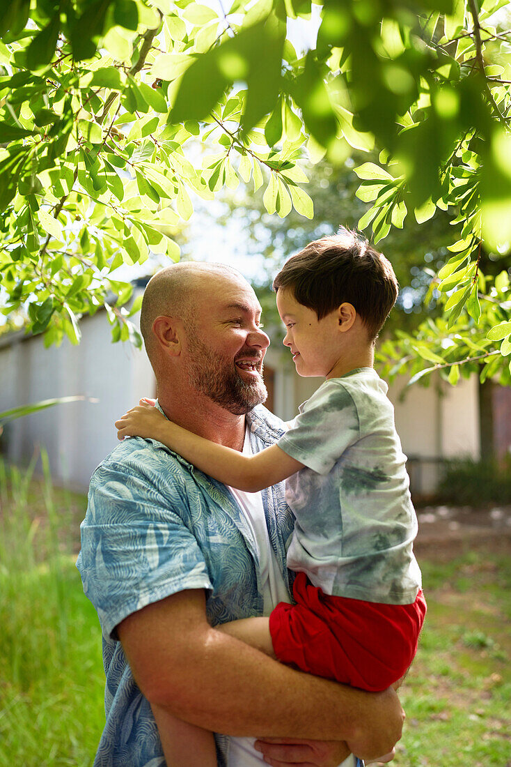 Father holding son with Down syndrome in backyard