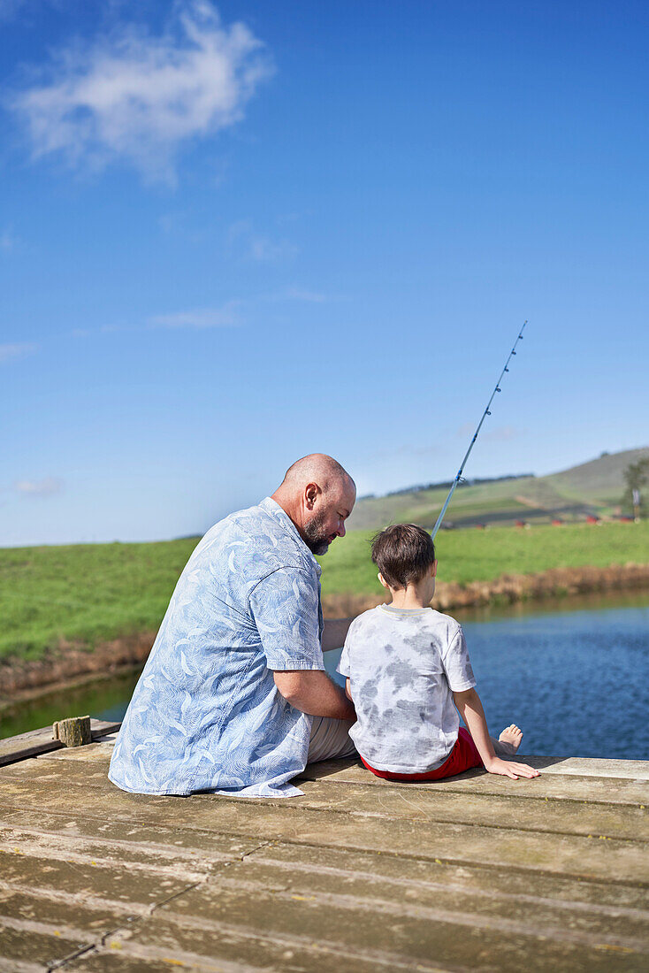 Father and son fishing on sunny lakeside dock