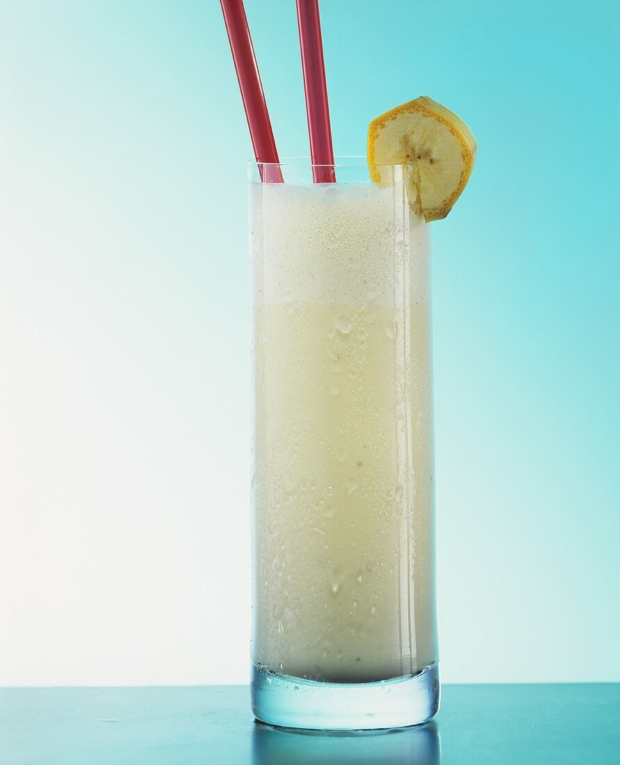 Banana milk shake in glass with straws and slice of banana