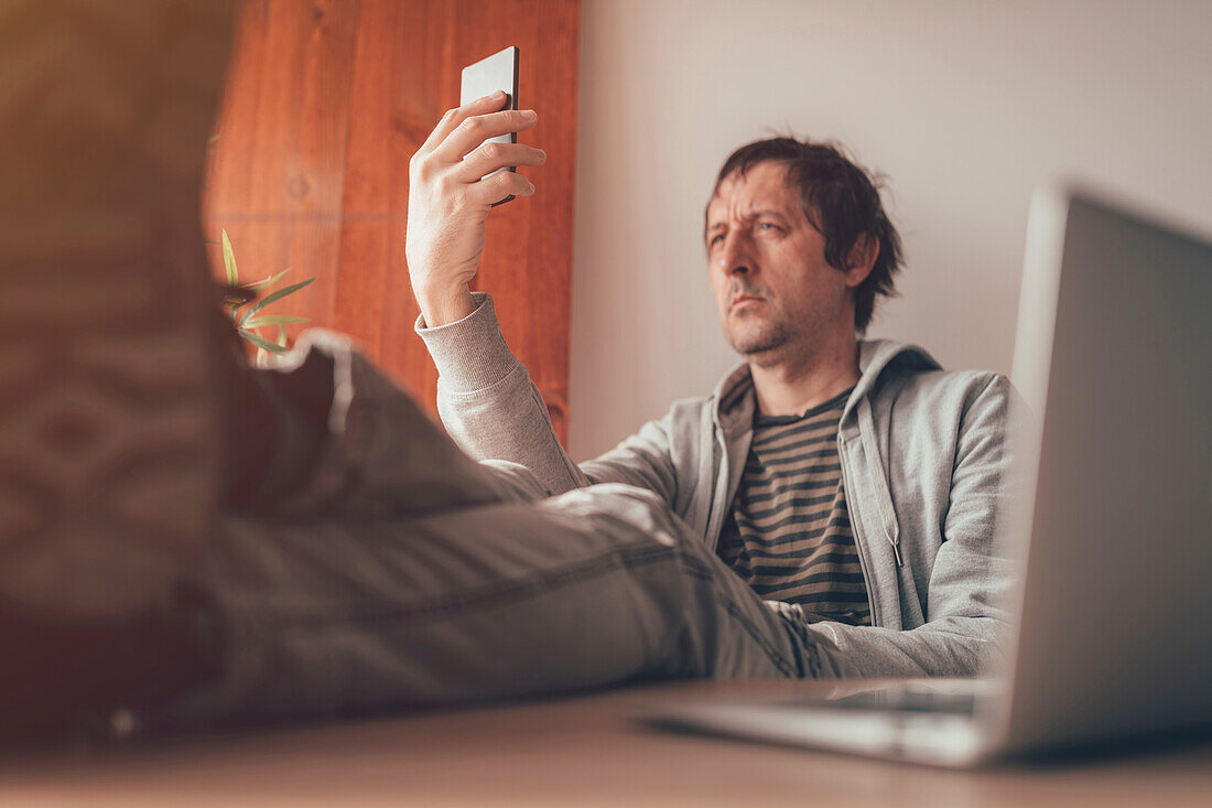 Man using smartphone with feet on desk