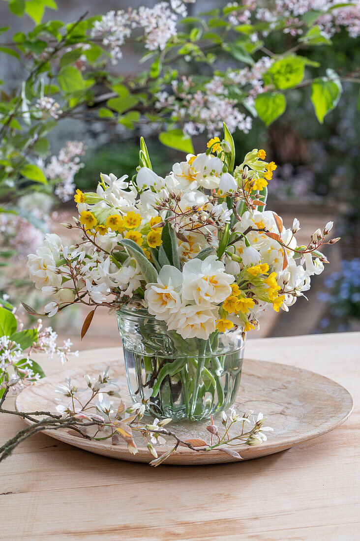 Blumenstrauß aus Schlüsselblume (Primula veris), Felsenbirne (Amelanchier), Narzissen 'Bridal Crown' (Narcissus) in Glasvase  auf Gartentisch