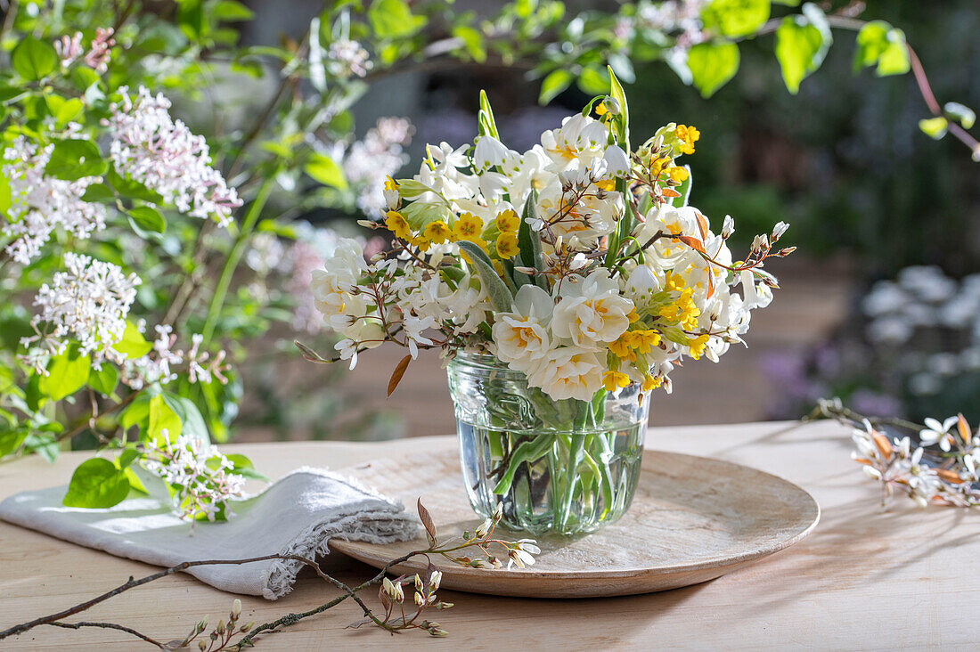 Blumenstrauß aus Schlüsselblume (Primula veris), Felsenbirne (Amelanchier), Narzissen 'Bridal Crown' (Narcissus) in Glasvase auf Gartentisch