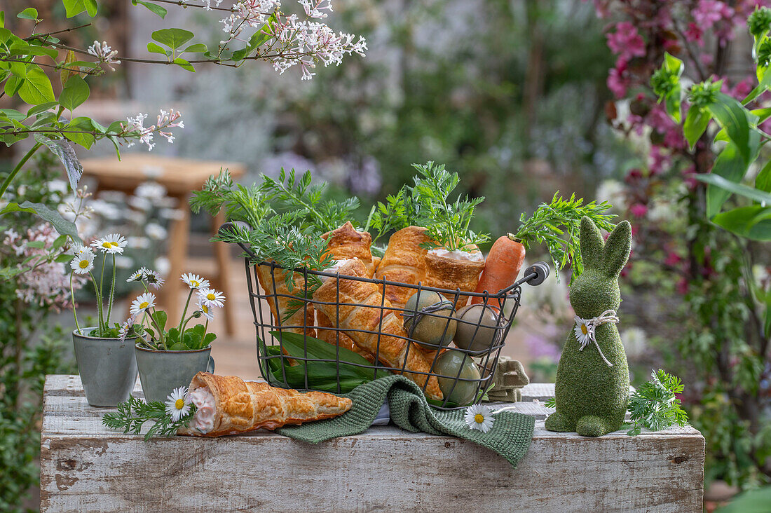 Puff pastry cones filled with carrot and dill sour cream in a wire basket and colored eggs, herbs as decoration, daisies in a cup as a vase, Easter bunny figurine