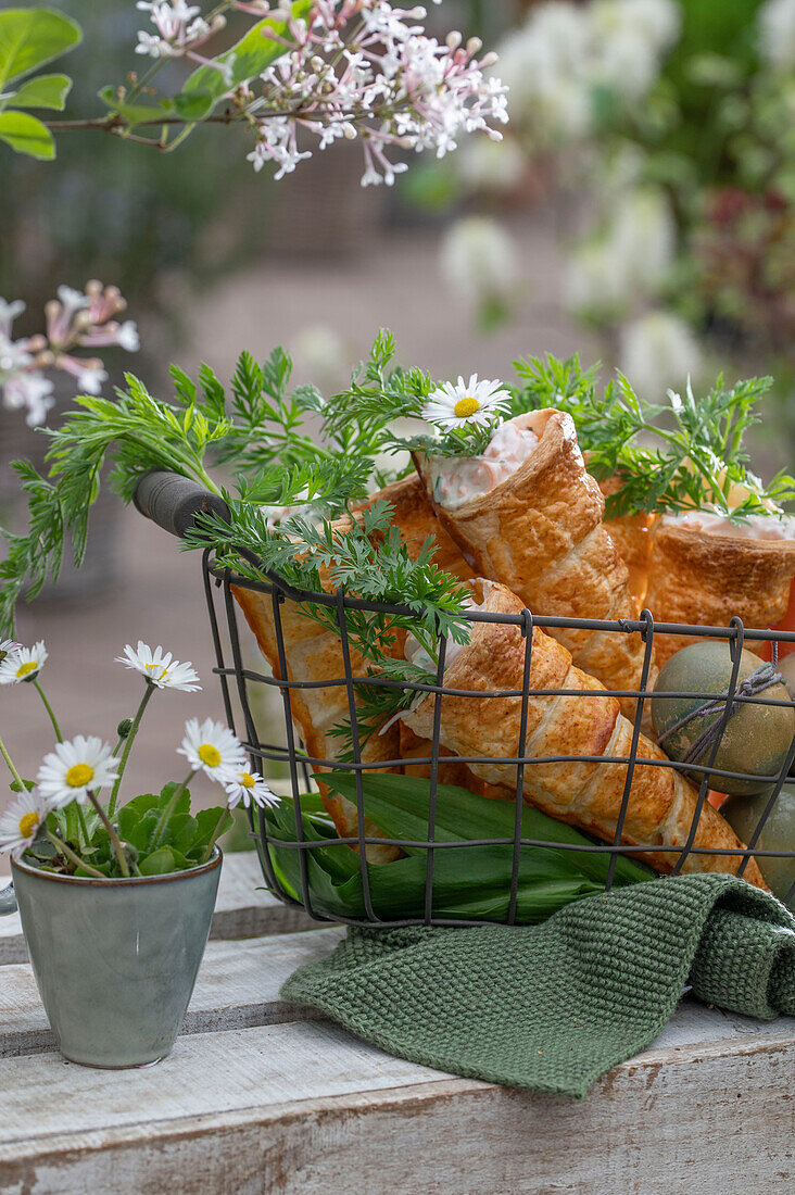 Puff pastry cones baked in the oven, filled with carrot, dill and sour cream sauce in a wire basket, herbs as decoration, daisies in a cup as a vase