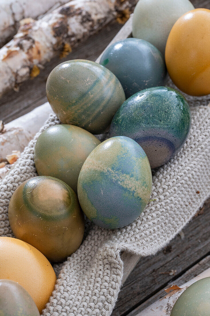 mit Naturfarben bunt gefärbte Ostereier in Holzkasten mit Strickdeckchen auf Birkenästen