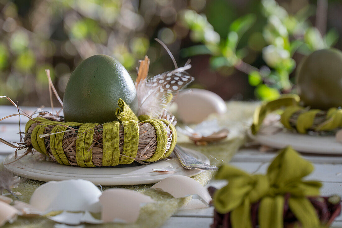 Osterei im Nest mit Federn und Eierschalen dekoriert auf Gartentisch