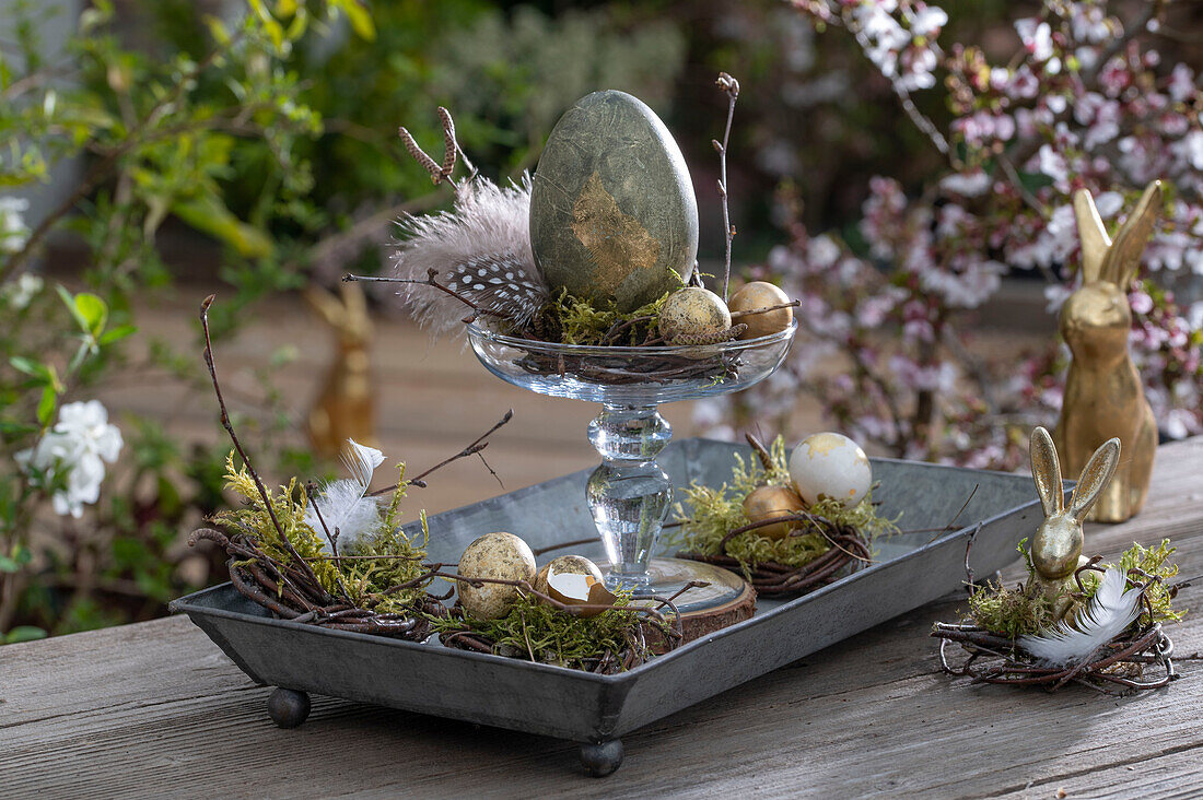 Etagere with golden Easter eggs and quail eggs, feathers and moss, bunny figures, Easter decoration