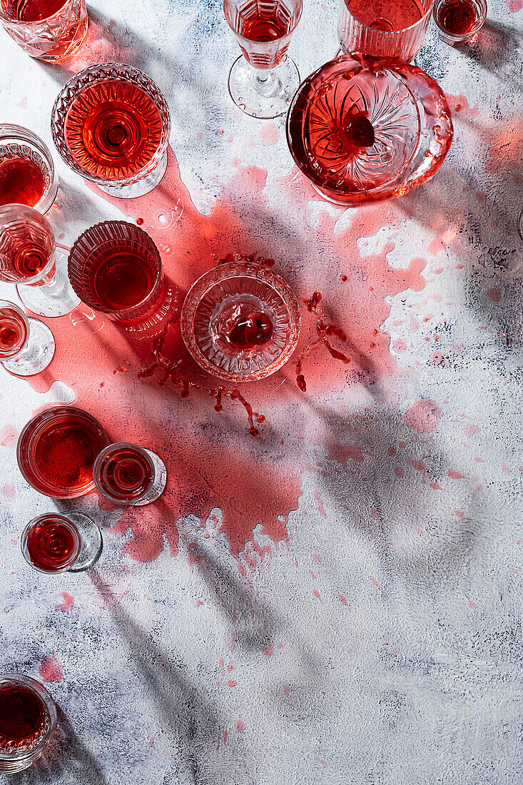 Roter Cocktail in verschiedenen Gläsern, teilweise verschüttet