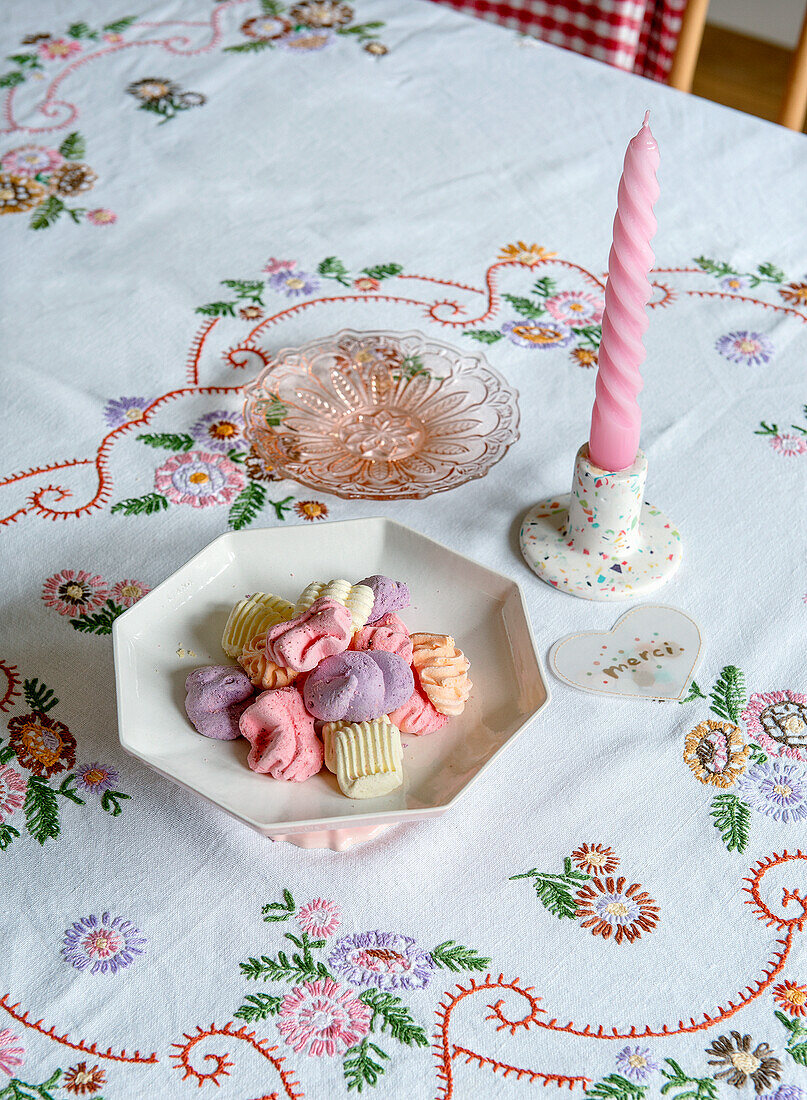 Embroidered tablecloth, pastries on a ceramic plate, a twisted candle in a candle holder next to it