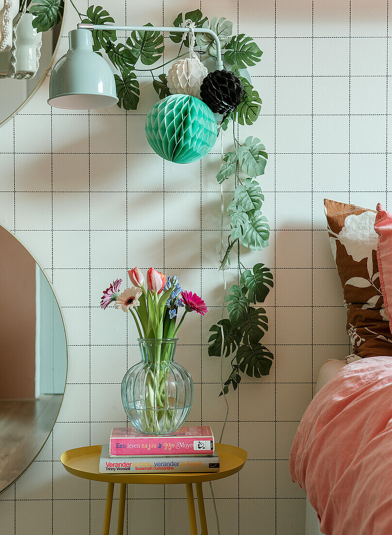 Bedside table with glass vase, books and wall decoration made of green leaves