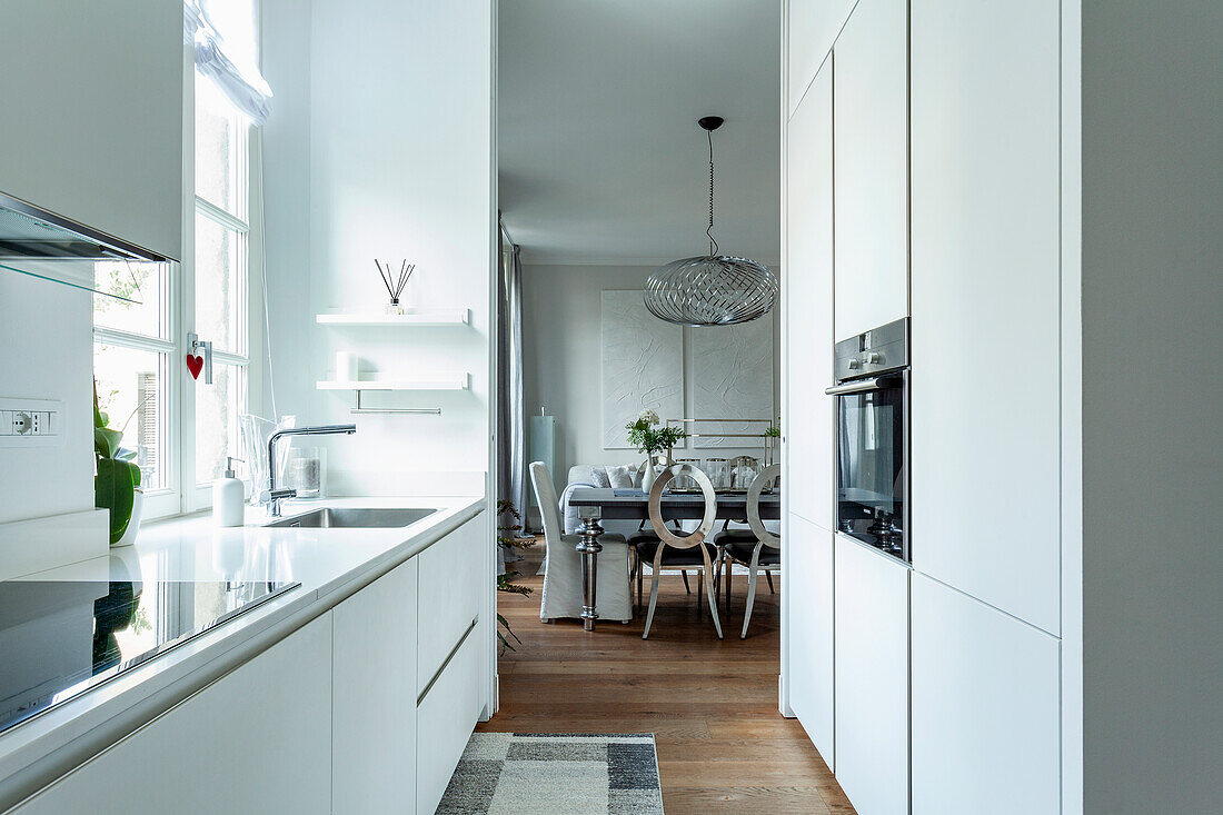 Modern, white kitchen with view of dining area and globe pendant light