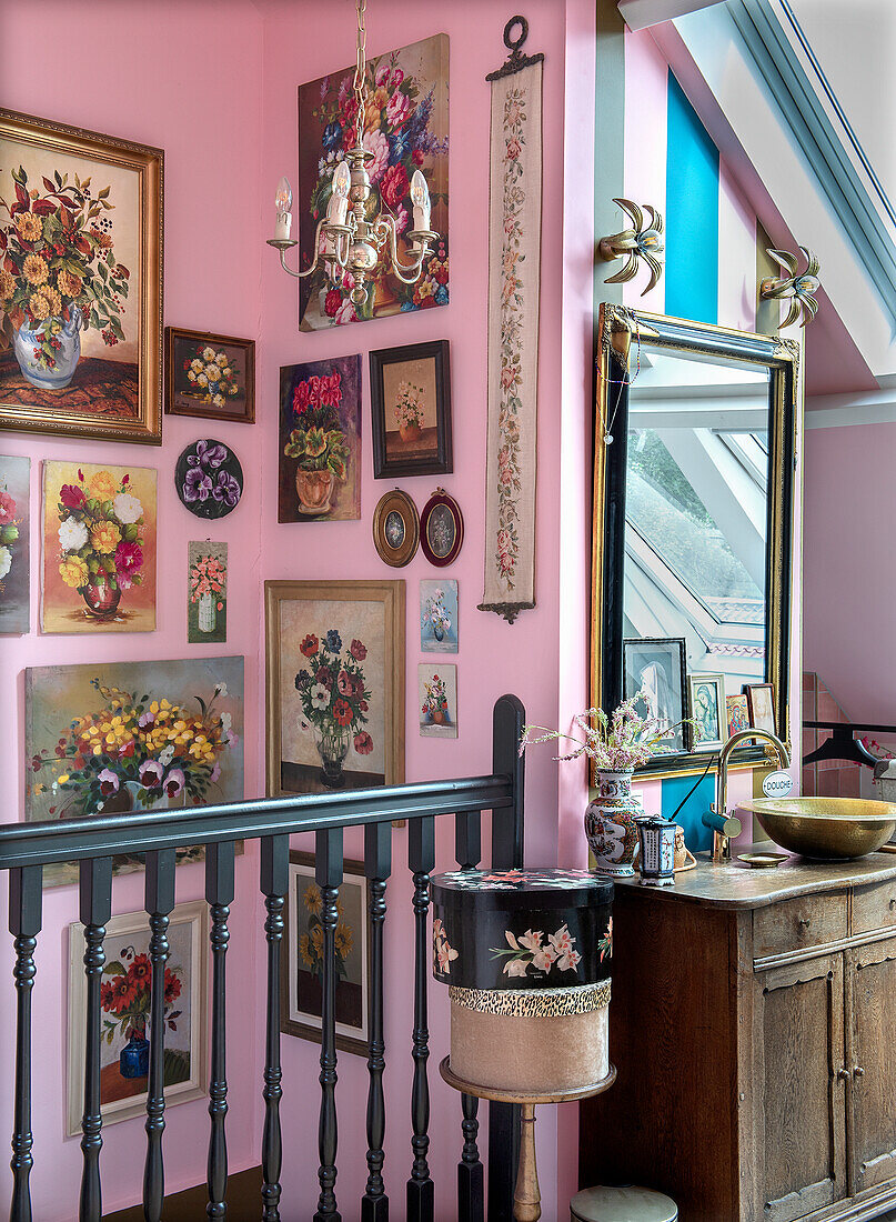 Treppenaufgang mit Blumengemälden und Vintage-Holzkommode vor rosa Wand