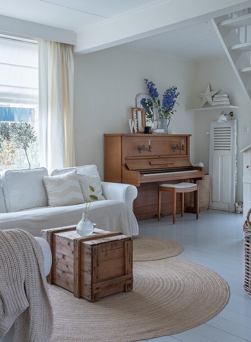 Living room with white sofa, vintage piano and rustic wooden chest