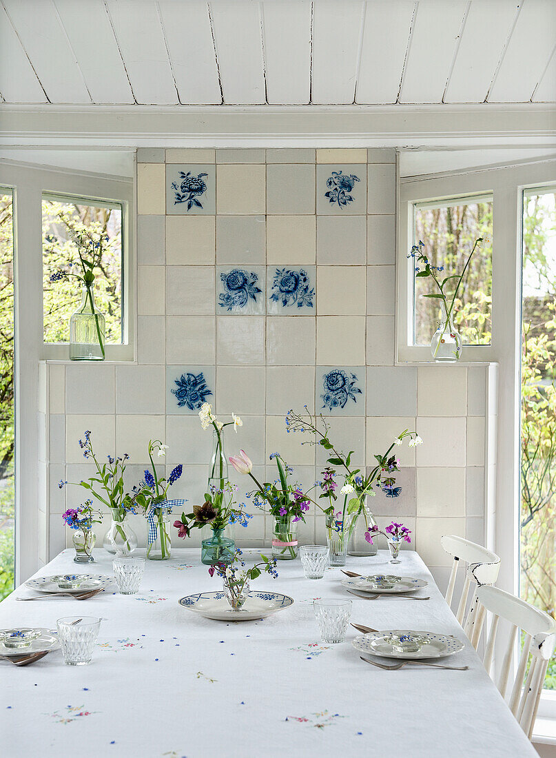 Gedeckter Esstisch mit Blumensträußen vor Kachelwand mit blauen Blumenmotiven