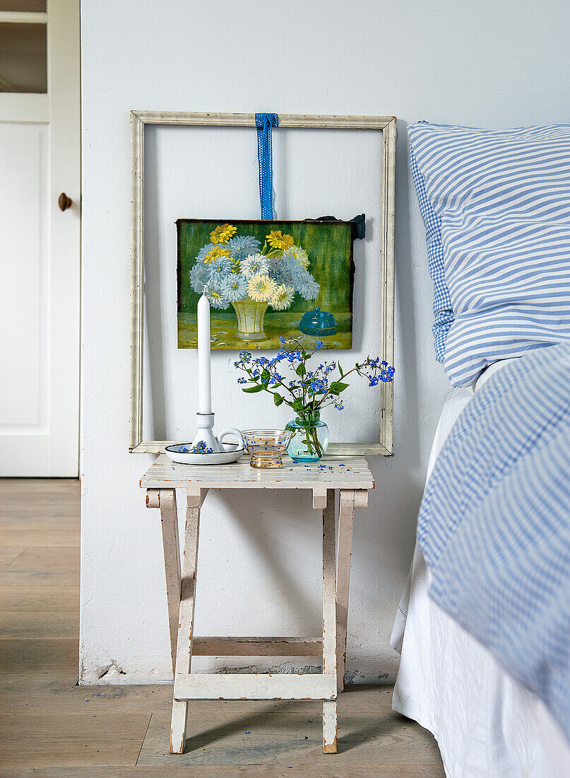 Nachttisch mit Kerze, Vase und Blumenbild im Schlafzimmer