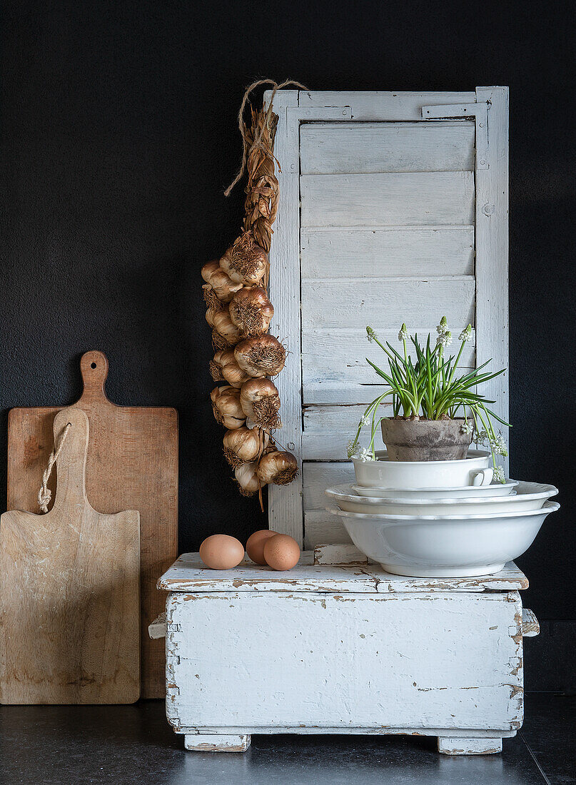 Vintage kitchen scene with boards, garlic braid, eggs and plant on a white wooden box