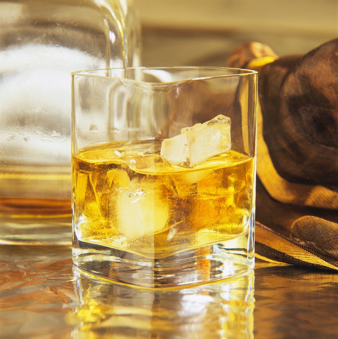 Whisky mit Eiswürfeln im Glas vor Whiskyflasche auf Tisch