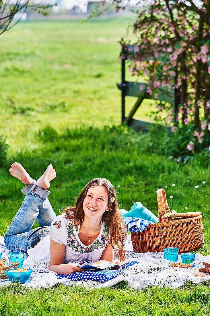 Junge Frau liest Zeitschrift auf Picknickdecke im Freien