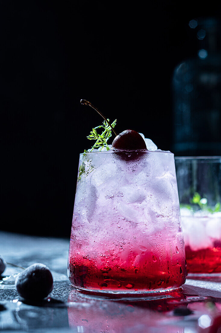 Refreshing summer drink with cherry and thyme sprig on ice