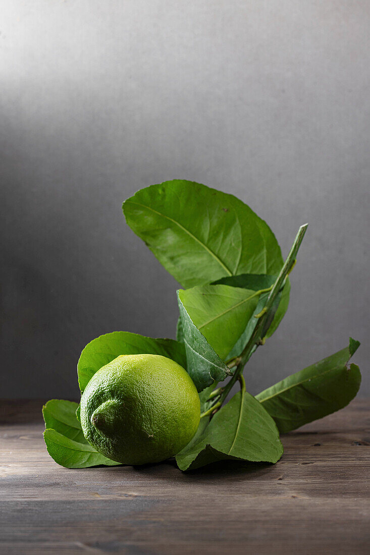 Green lemon with leaves on wooden surface
