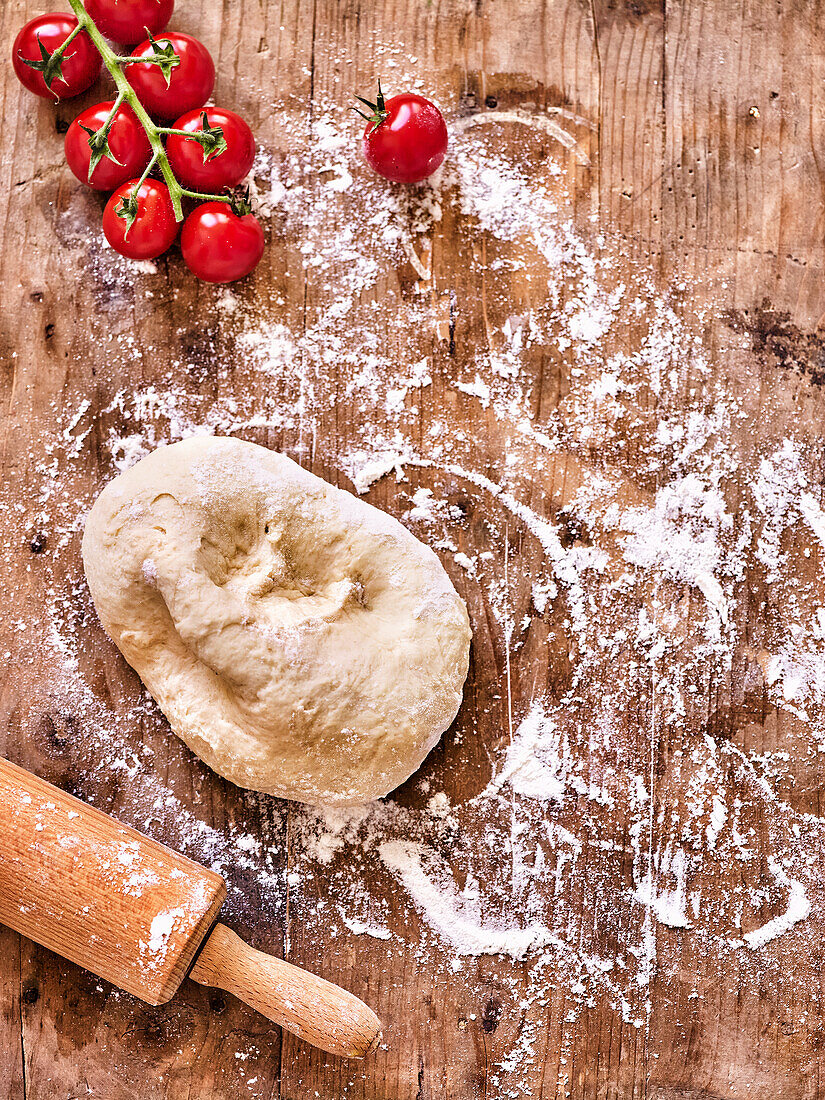 Pizza dough, floured work surface, rolling pin, cherry tomatoes