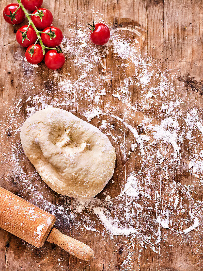 Pizzateig, bemehlte Arbeitsfläche, Nudelholz, Kirschtomaten