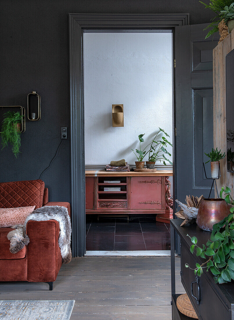 Living room with rust-brown velvet sofa and view of antique red chest of drawers in the hallway