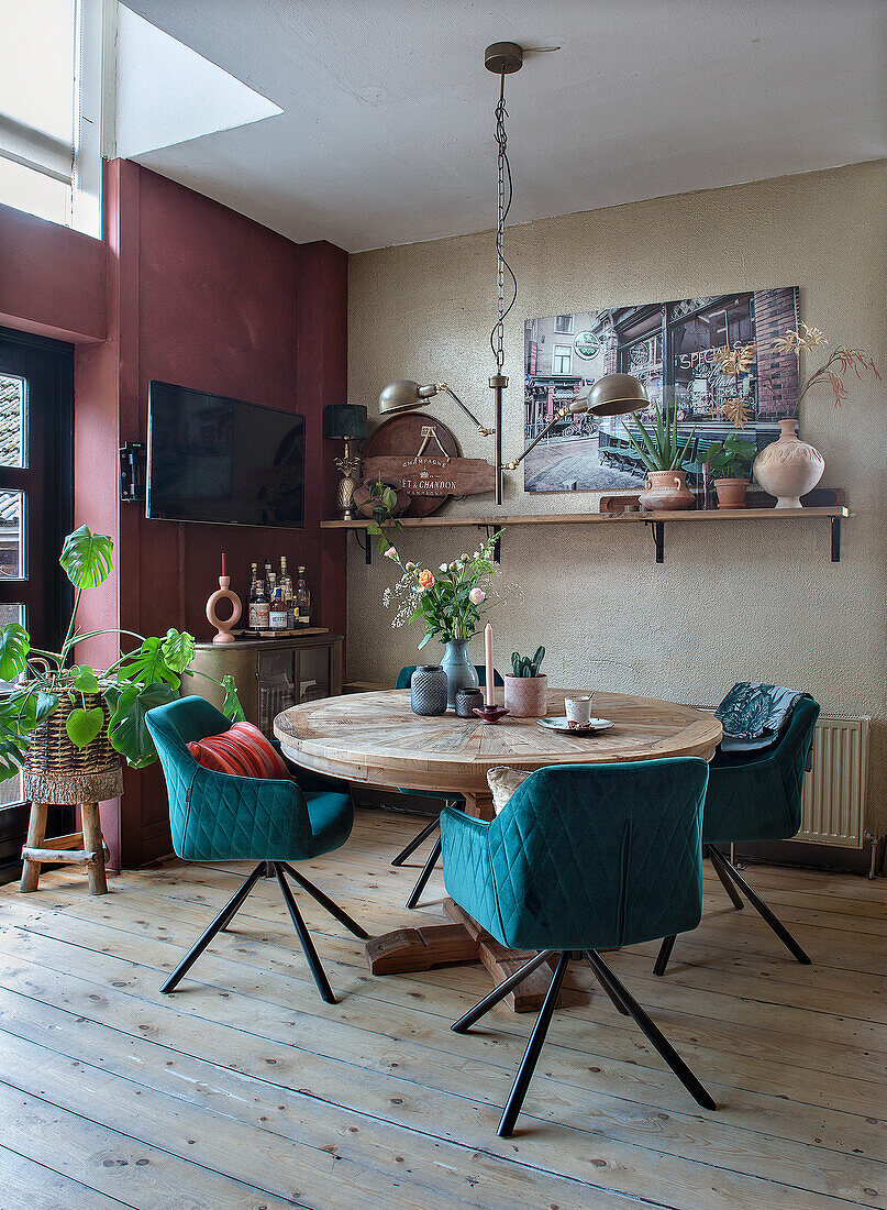 Modernes Esszimmer mit rundem Holztisch mit blauen Samtstühlen mit Holzboden und Regal