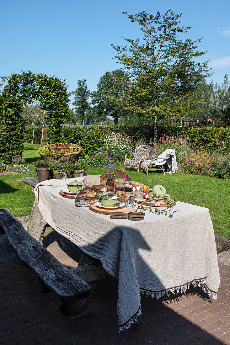 Gedeckter Gartentisch mit rustikalem Holzbänkchen im üppigen Garten