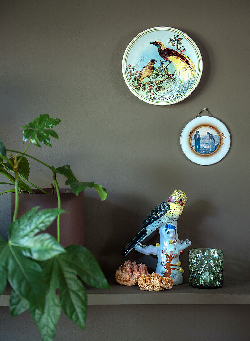 Shelf with porcelain bird figurine, decorative wall plates and potted plant