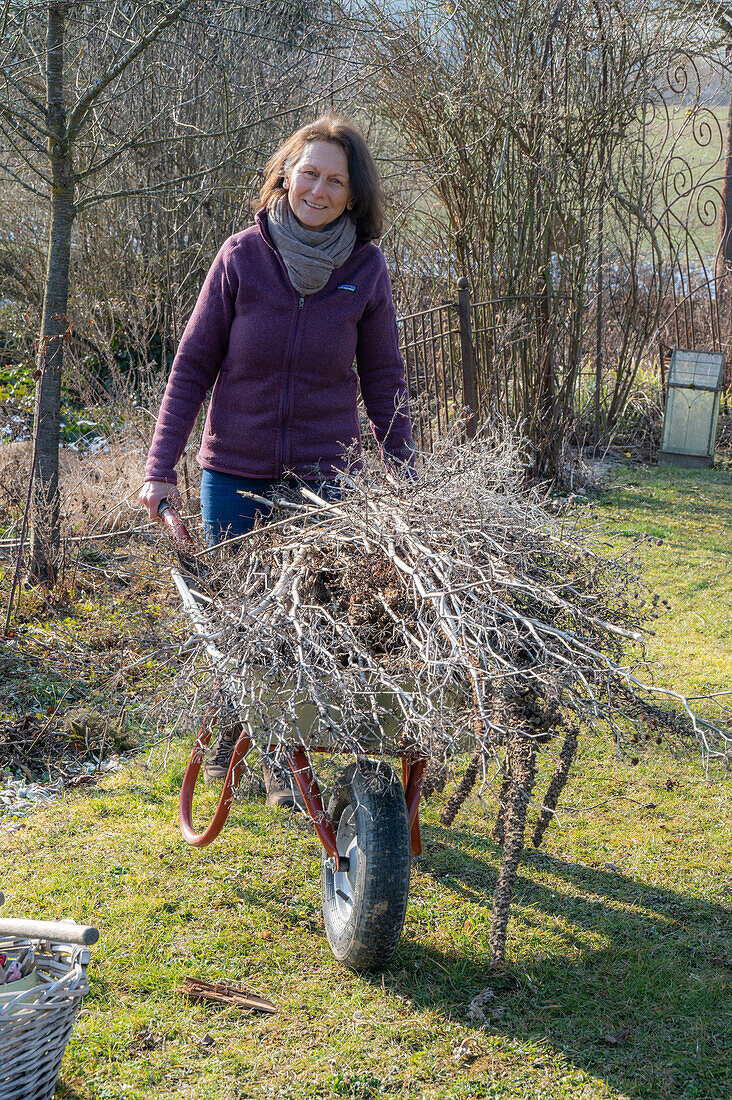 Frau bei der Gartenarbeit mit Schubkarren, Bäume zuschneiden
