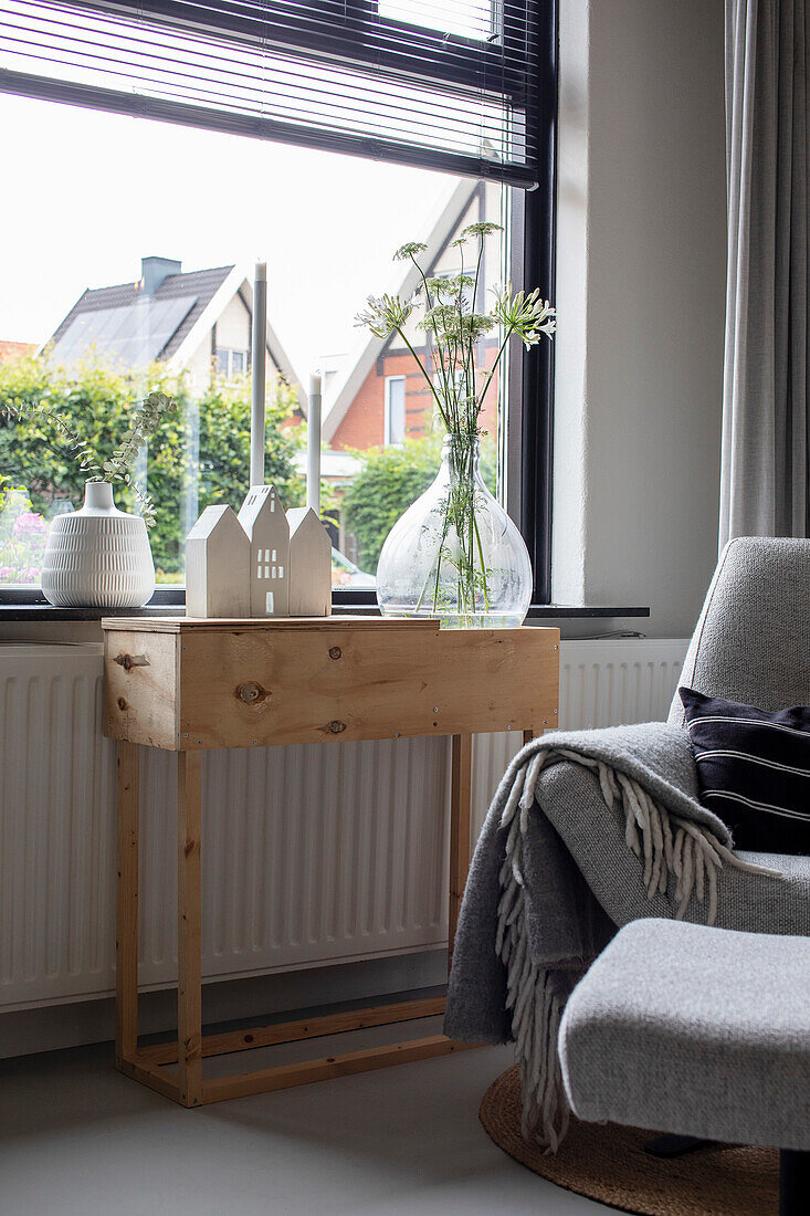 Holzbeistelltisch im Wohnzimmer mit Dekoration und Glasvase am Fenster