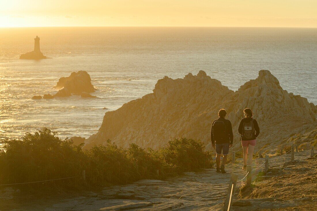 France,Finistere,Plogoff,hiker at sunset at Pointe du Raz,the lighthouse of the Vieille in background