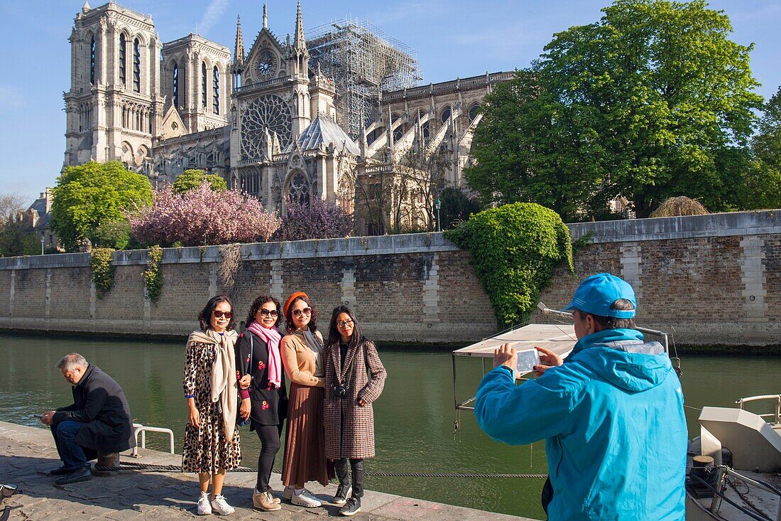 France,Paris,Notre Dame de Paris Cathedral,two days after the fire,April 17,2019,Asian tourists being photographed in front of the cathedral from the quay of Montebello