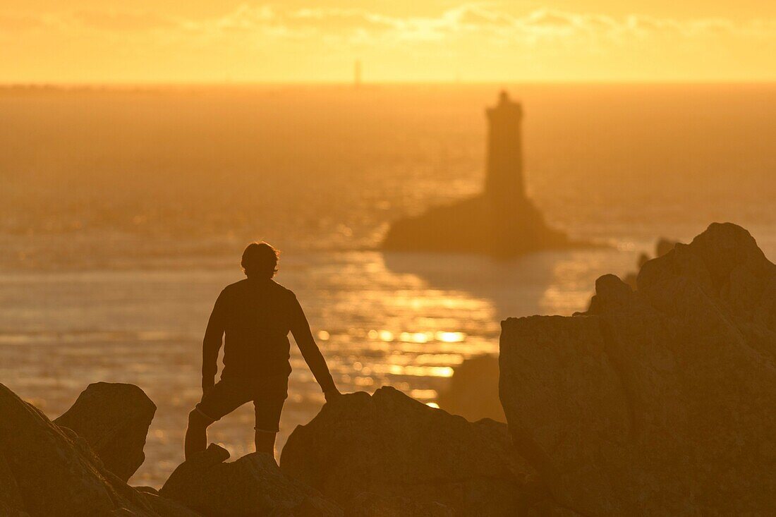 France,Finistere,Plogoff,hiker at sunset at Pointe du Raz,the lighthouse of the Vieille in background
