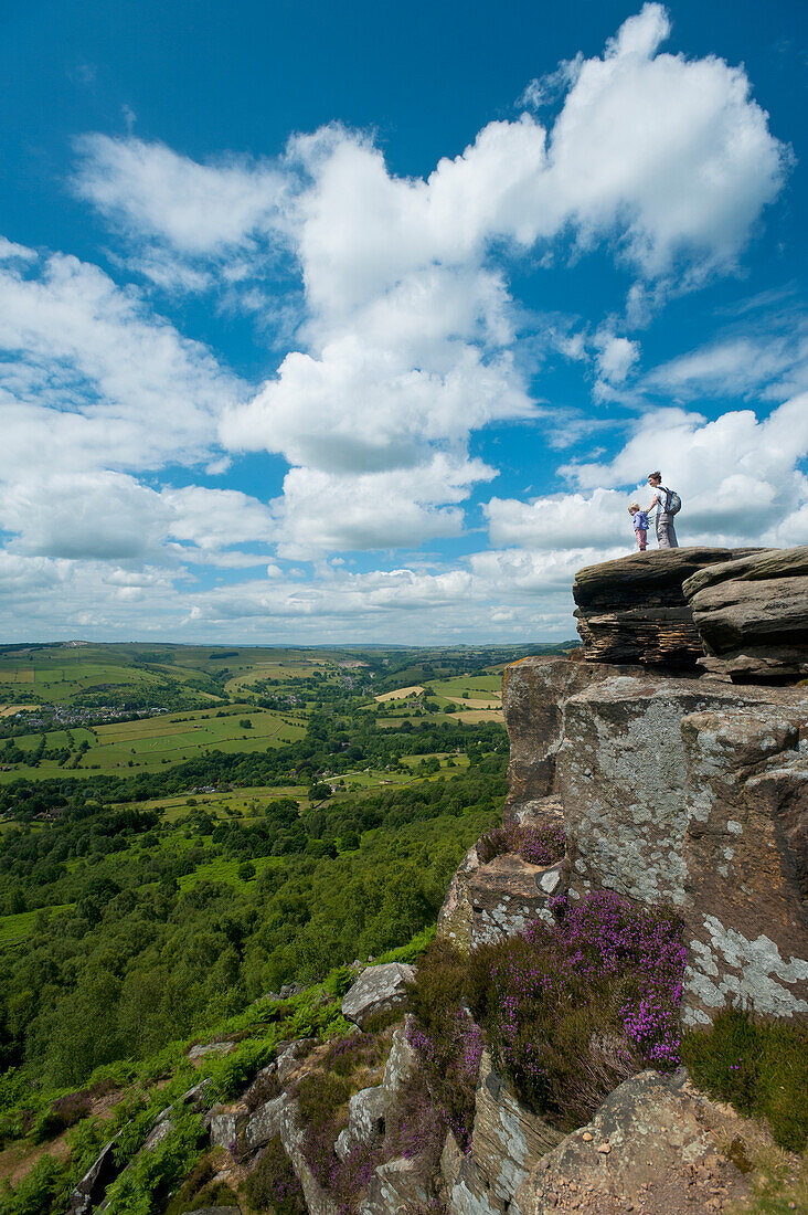 UK,Derbyshire,Mother and young girl sitting on rocks admiring view at Froggatt Edge across Peak District,Froggatt