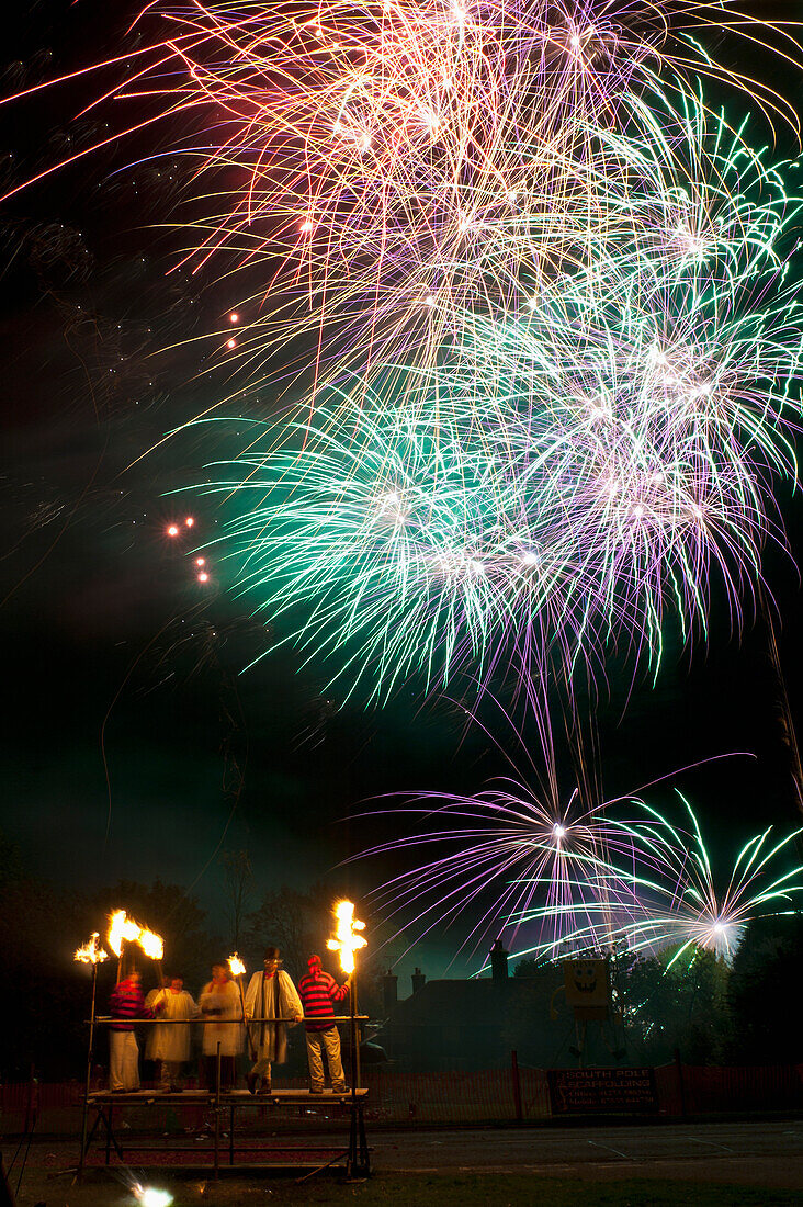 UK,England,Als Geistliche verkleidete Menschen auf einer Tribüne mit Feuerwerkskörpern im Hintergrund bei der Newick Bonfire Night, East Sussex