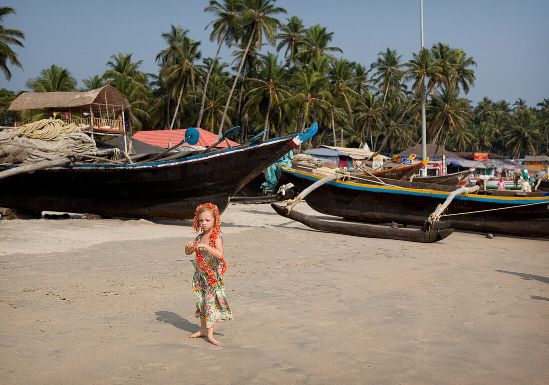 Isla Reynolds 4 years old stands in front of the many traditional boats and beach front restaurants that line Palolem beach,Goa,India.