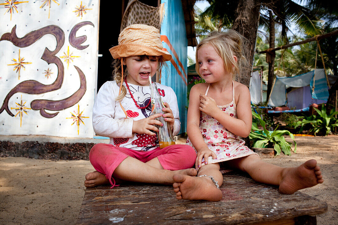 Mädchen trinken Saft durch einen Strohhalm auf einem Tisch, Patnum, Goa, Indien.