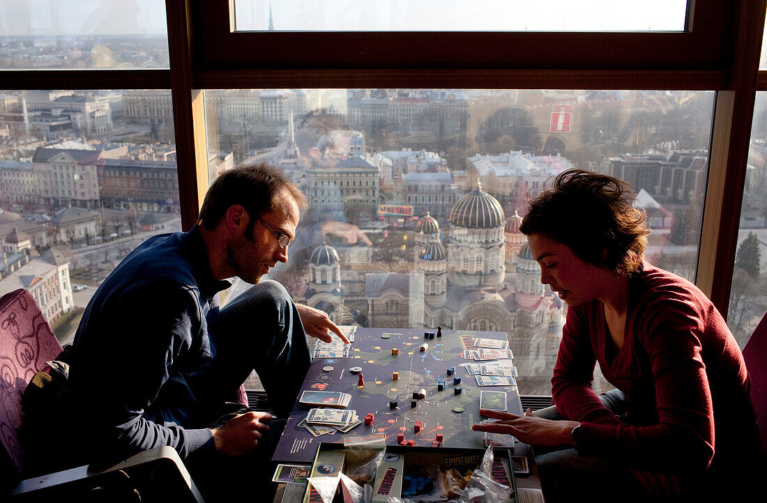 Besucher spielen ein Brettspiel im 26. Stock der Skyline Bar des Reval Hotels, bei Sonnenuntergang, Riga, Lettland.