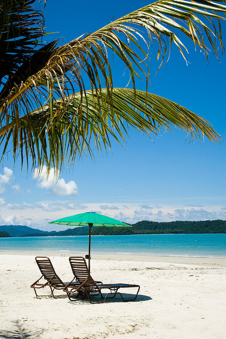 Deck Chairs Under Parasol On White Sandy Beach With Palm Trees Overlooking Blue Sea. Pantai Cenang (Cenang Beach),Pulau Langkawi,&#10,Malaysia,South East Asia.