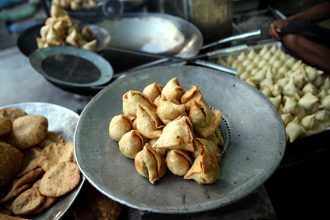 Detail von Samosa indischen Snacks und anderen indischen frittierten Snacks, einschließlich Puri, indisches frittiertes Brot, an der Vorderseite dieses Lebensmittel-Cafés in Varanasi. Die Kultur von Varanasi ist eng mit dem Fluss Ganges und seiner religiösen Bedeutung verbunden.