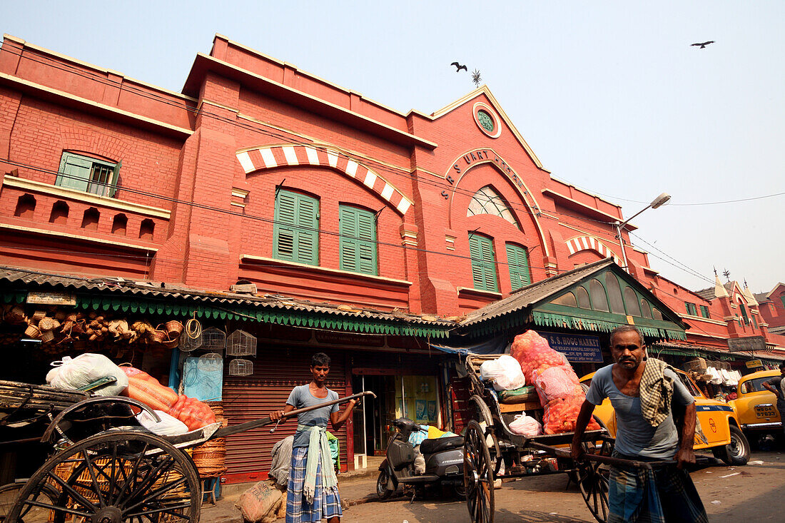 Menschliche Rikschas transportieren Waren auf dem berühmten New Market in der Nähe der Sudder Street, einem beliebten Viertel für preiswerte Unterkünfte für Rucksacktouristen in Kalkutta / Kolkata, der Hauptstadt des Bundesstaates Westbengalen, Indien, Asien.