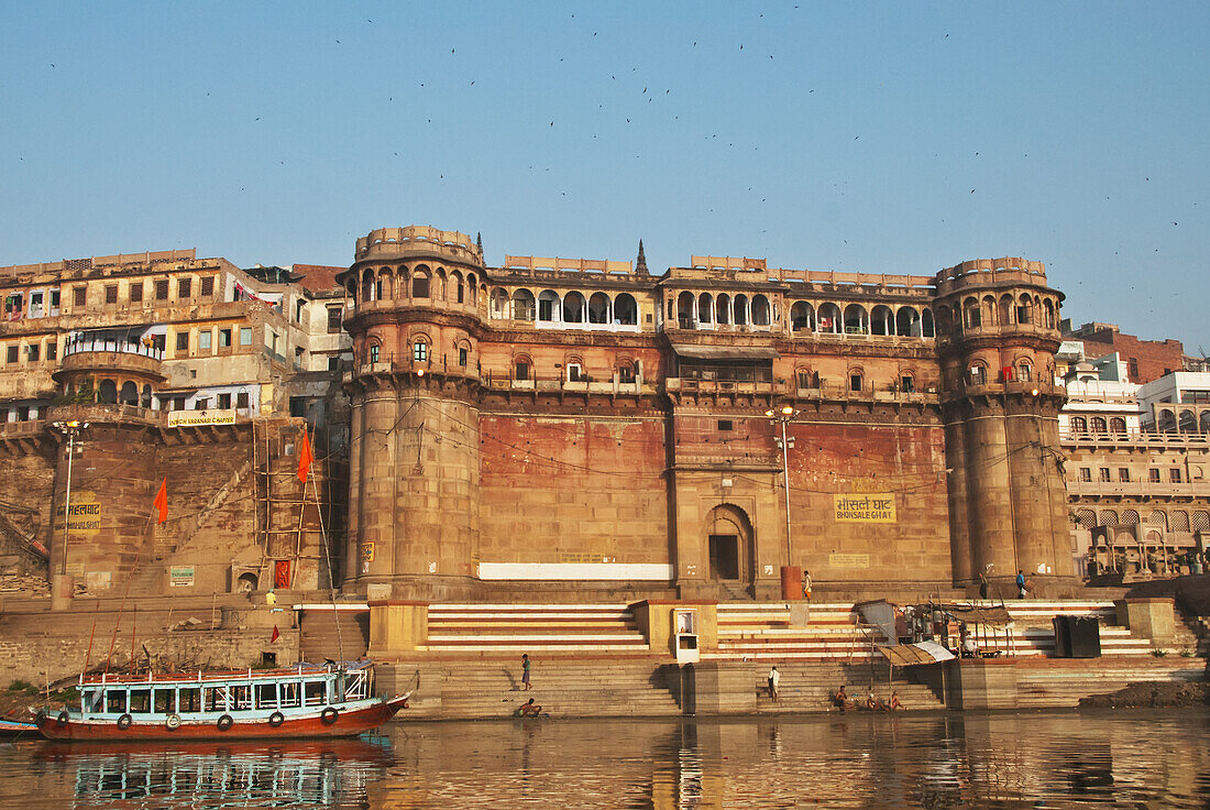 Indien, Uttar Pradesh, aufgenommen von einem Boot auf dem Ganges, Varanasi, Bonsale Ghat mit blauem und rotem Holzboot