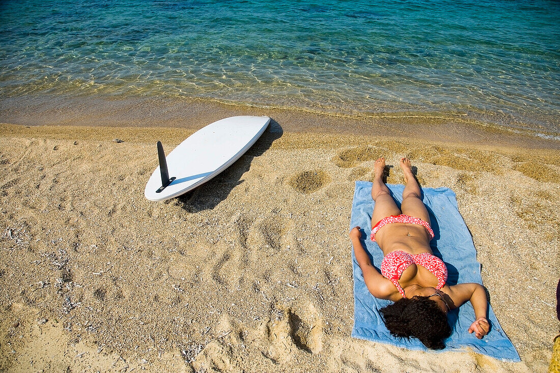 Greece,Halkidiki,Young woman sunbathing on beach with surf board on sand,Ierissos