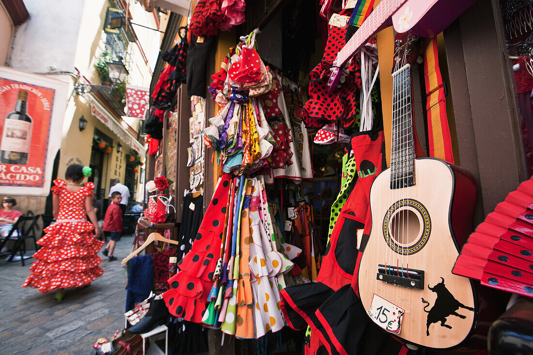 Mädchen in traditioneller sevillanischer Kleidung im Vorbeigehen an einem Souvenirladen in der Altstadt, Santa Cruz, Sevilla, Andalusien, Spanien