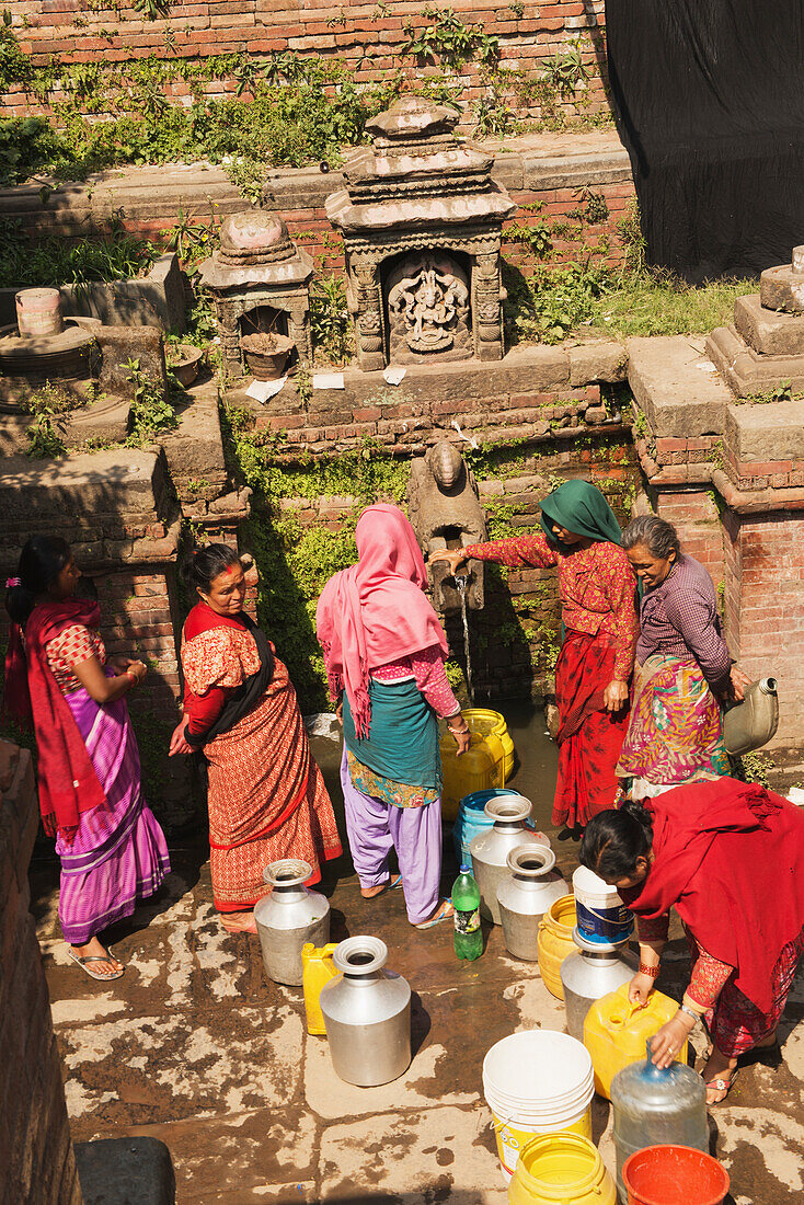 Frauen in bunten Saris füllen Wasserbehälter aus einem Wassertrog in einem alten Tank auf,Bhaktapur,Nepal