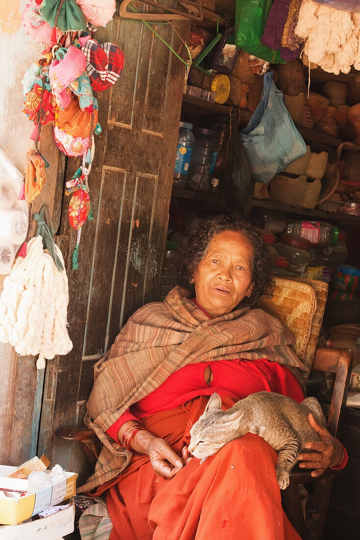 Alte Newar-Frau in traditioneller Kleidung hält ihre Katze in der Eingangstür ihres Ladens, Bhaktapur, Nepal